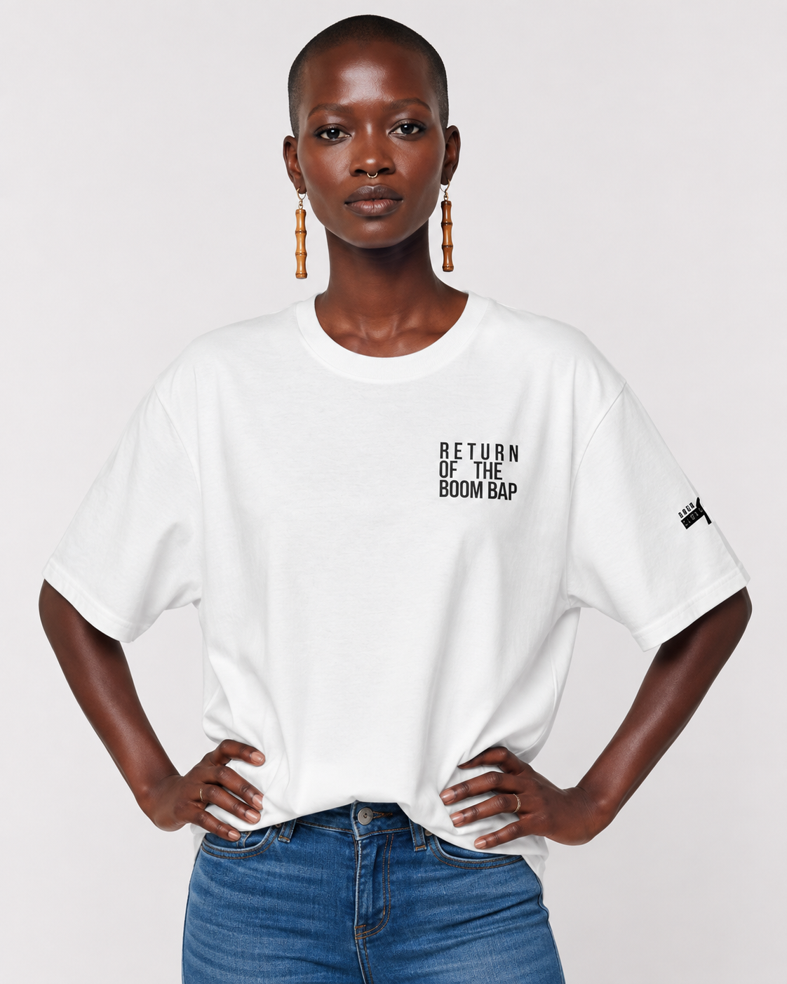 Front White A model wearing a white short-sleeve t-shirt with black text reading 'RETURN OF THE BOOM BAP' on the left chest, paired with blue jeans against a light gray background.